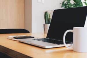 Laptop used to do chemical hygiene plan authoring on desk with mobile phone and coffee cup